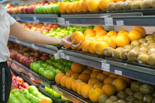 Fresh healthy fruits on shelves in supermarket. With a woman hand choosing best fruits