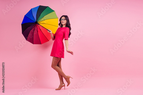 beautiful brunette girl in the studio on a pink background in the style dress with rainbow an umbrella
