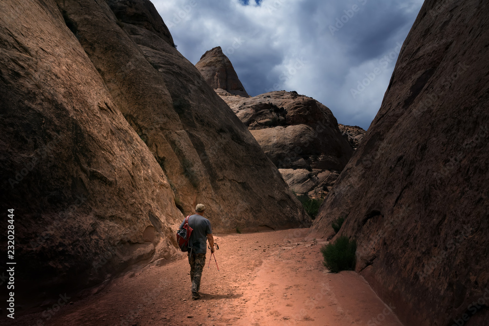 Traveler with a backpack goes through the canyon. Clouds. Capitol Gorge Trail, Capitol Reef National Park, Utah, USA