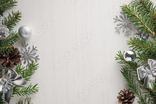 Green spruce twigs, pine cones and silver Christmas decorations on white background with copy space