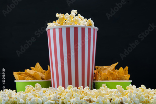 bar snack for a cinema, on a black background a bucket of nachos and a glass of popcorn