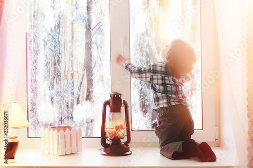 A child in the new year looks out the window. Children are waiting for Santa Claus. A child in a Santa suit sits at the window.