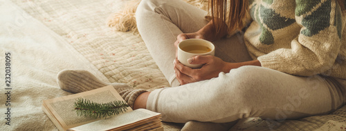 Cozy home. Beautiful girl is reading a book on the bed. Good morning with tea. Pretty young girl relaxing. The concept of reading