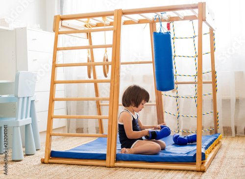 A small child is engaged in boxing on a wooden home sports complex. Girl in boxing gloves hits the pear. Children's physical development. photo