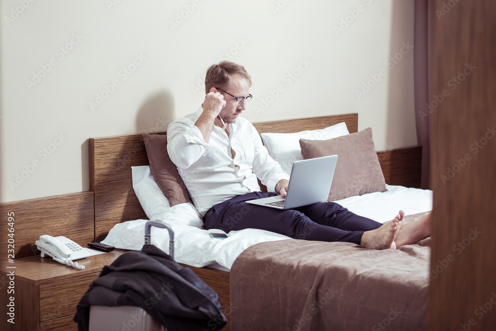 Blonde-haired businessman using earphones for video chat in hotel room
