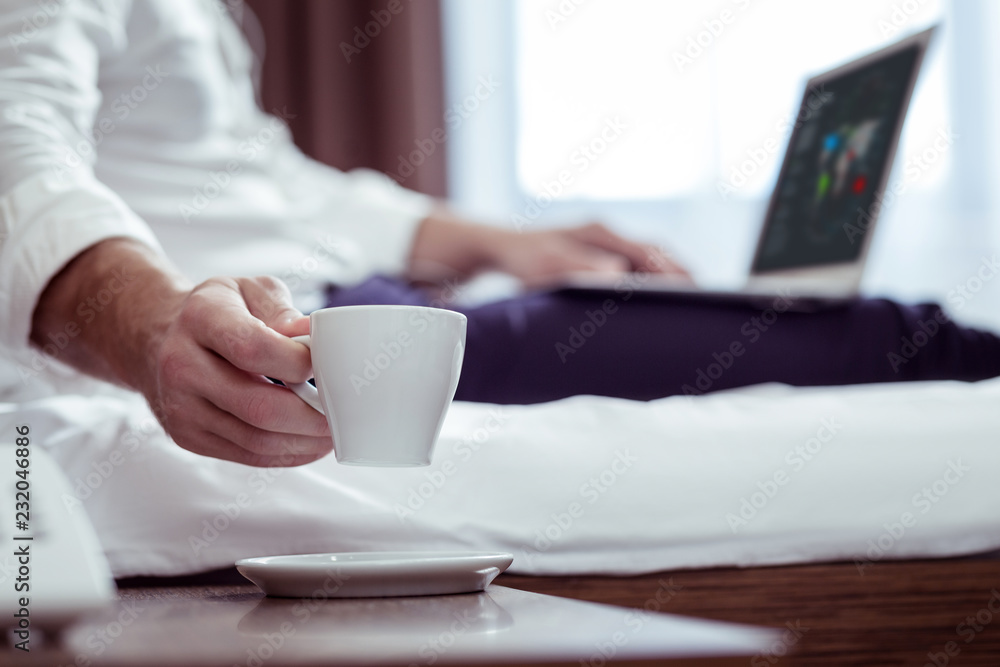 Businessman wearing suit lying on bed while drinking some tea Businessman wearing suit lying on bed while drinking some tea