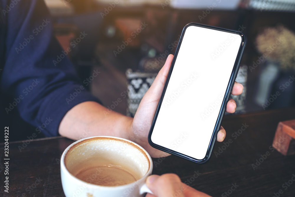 Mockup image of a woman holding and showing black mobile phone with blank screen to someone on the table in cafe Mockup image of a woman holding and showing black mobile phone with blank screen to someone on the table in cafe