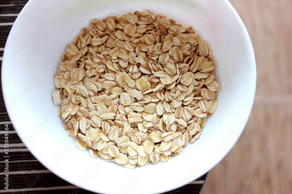 Oat flakes in a white bowl on brown Oat flakes in a white bowl on brown