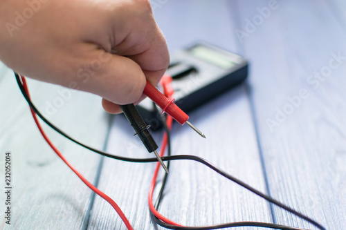 Electronic multimeter to measure the current in a male hand on a wooden background.