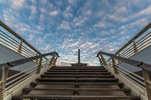 Abstract picture of a wooden staircase going up to the regular blue clouds shape sky
