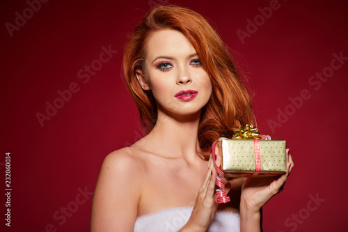 Happy excited young woman in santa claus costume with gift box over red background