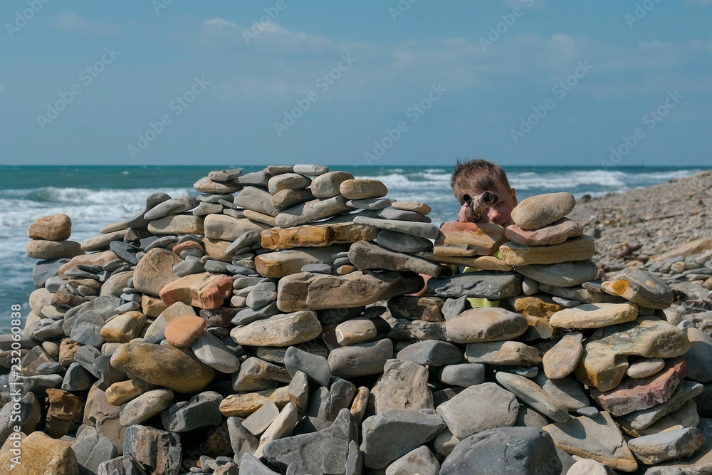 Boy playing, hiding behind a fortress of stones on the sea shore beach. Boy playing, hiding behind a fortress of stones on the sea shore beach.