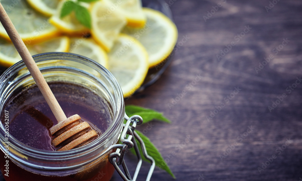 Tea with lemon and mint in nature. A cup of hot mint tea with lemon and honey in a jar. Lemon slices and a spoon with honey to hot tea. Tea with lemon and mint in nature. A cup of hot mint tea with lemon and honey in a jar. Lemon slices and a spoon with honey to hot tea.