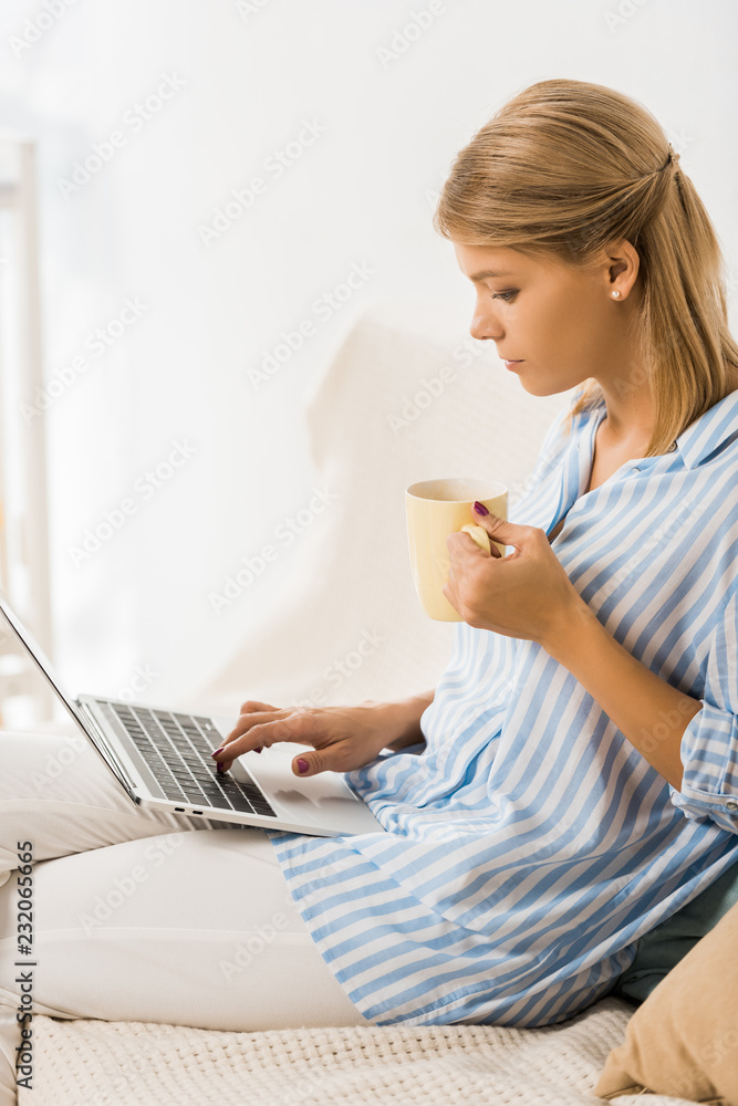 Fototapeta premium side view on adult woman holding cup of tea and using laptop