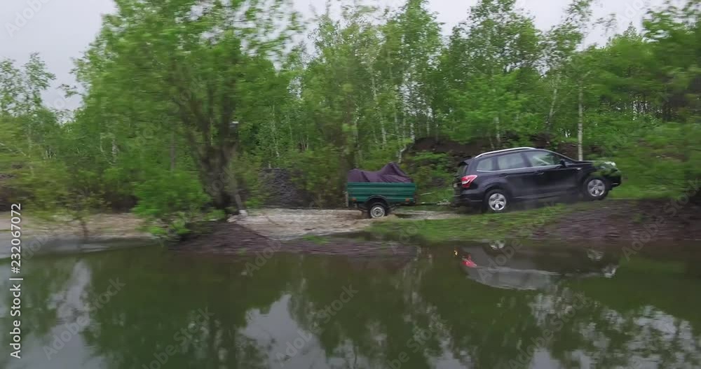One black SUV with trailer driving on winding dirty road in forest mountains - Aerial Drone View One black SUV with trailer driving on winding dirty road in forest mountains - Aerial Drone View