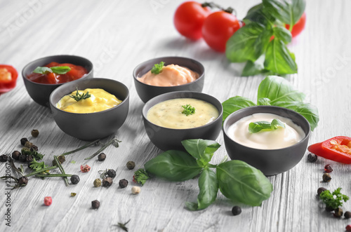 Different tasty sauces in bowls with spices on light wooden table photo