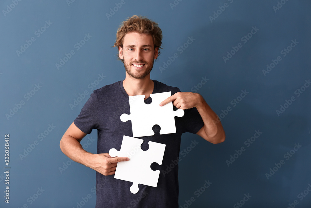 Young man with pieces of jigsaw puzzle on color background Young man with pieces of jigsaw puzzle on color background