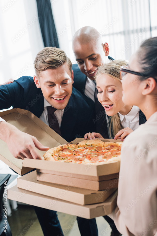 happy young coworkers looking at tasty pizza in office