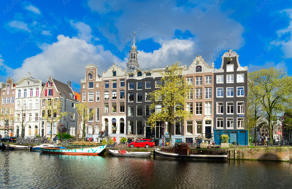Facades row of old historic Houses over canal water with spring green trees, Amsterdam, Netherlands