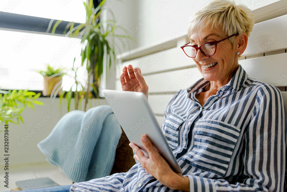 Smiling beautiful senior woman using digital tablet at home - obrazy, fototapety, plakaty 