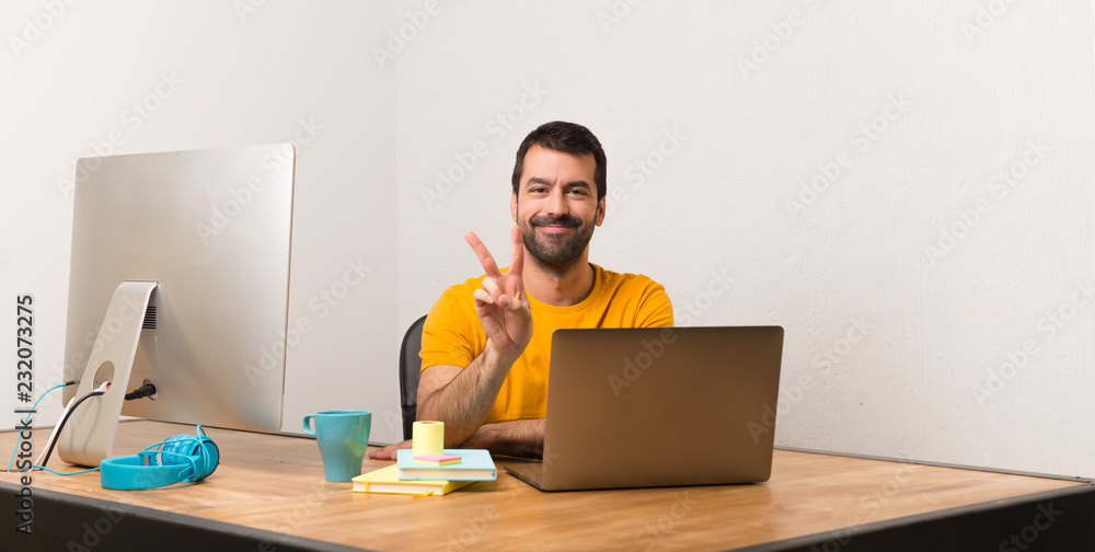 Man working with laptot in a office smiling and showing victory sign Man working with laptot in a office smiling and showing victory sign
