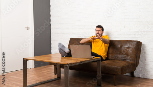 Man with his laptop in a room is a little bit nervous and scared stretching hands to the front