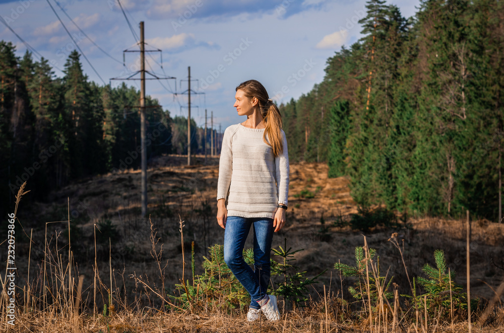 Woman in white knitted sweater posing against the backdrop of a forest clearing in the countryside Woman in white knitted sweater posing against the backdrop of a forest clearing in the countryside