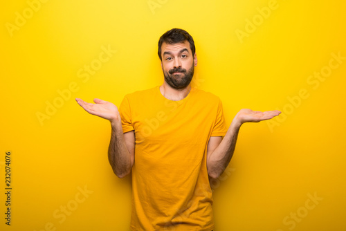 Man on isolated vibrant yellow color having doubts while raising hands and shoulders