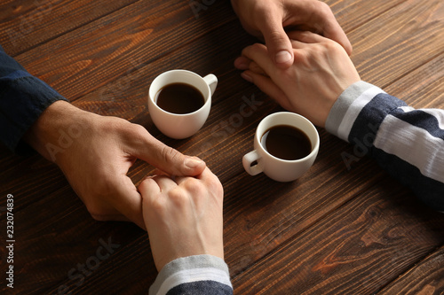 Loving young couple with cups of coffee on wooden background