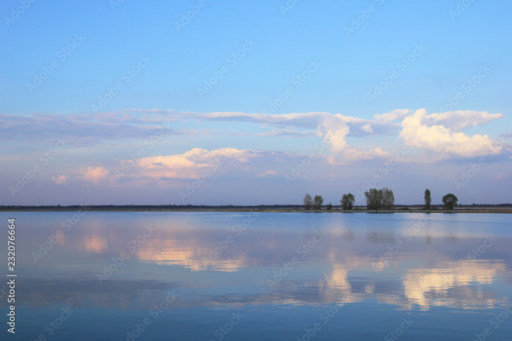 Beautiful lake in the evening, clouds reflect in water, trees on opposite bank