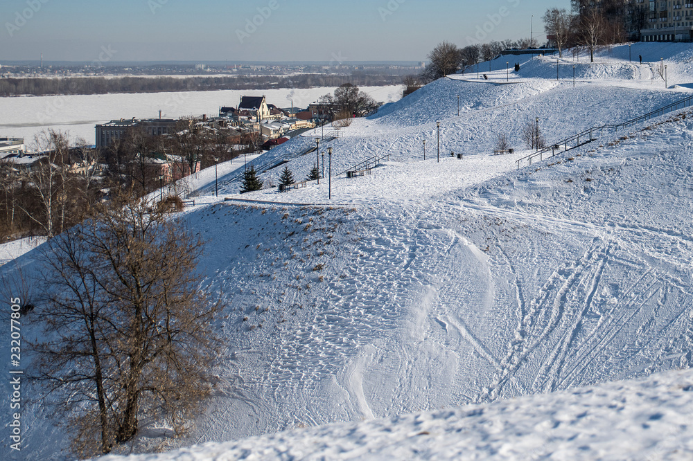 snowy urban slope against the background of a frozen river