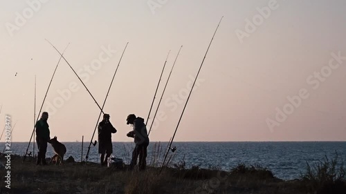 Few fishermen and the dog standing on the coast near the sea; one of them is casting the fishing rod. photo