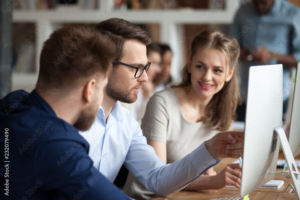 Fototapeta premium Diverse millennial employees coworking discussing business project or idea in shared office, smiling colleagues work together at pc, male worker explain to coworkers pointing at computer screen