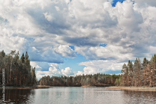 Beautiful volumetric clouds on a sunny day over a quiet forest lake