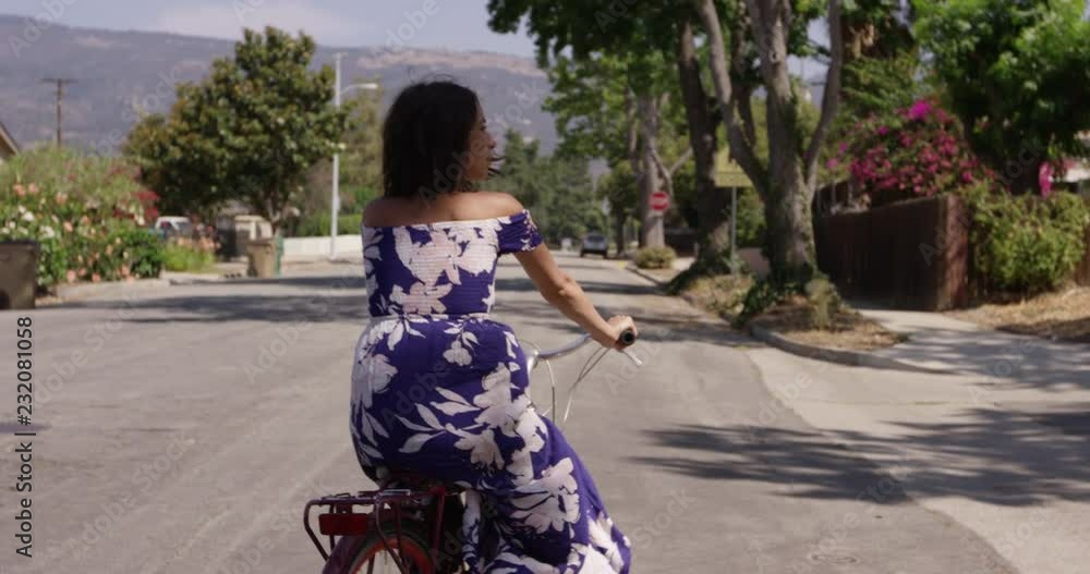 Stylish millennial woman riding bike through streets with mountains in the background Stylish millennial woman riding bike through streets with mountains in the background