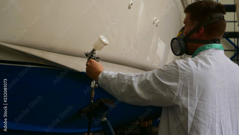 A young man (guy) is a specialist in cleaning the yacht, in a respirator and using a spray on the background of the yachts. Concept from: Professional, Specialist, Cleaning, Yacht service, Preparation A young man (guy) is a specialist in cleaning the yacht, in a respirator and using a spray on the background of the yachts. Concept from: Professional, Specialist, Cleaning, Yacht service, Preparation