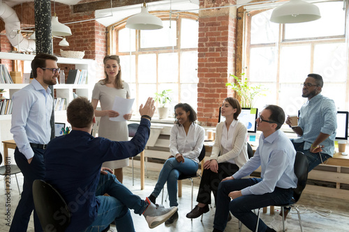 Ambitious male employee raise hand ask question to female presenter at meeting, man show activity at teambuilding with multiethnic colleagues, diverse workers brainstorm at office education briefing photo
