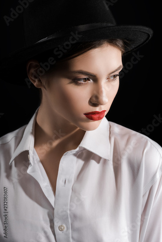 portrait of fashionable model in white shirt and black hat isolated on black
