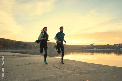 Young man and woman out for a run on the lake at the sunrise