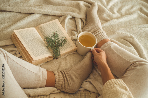 Cozy winter evening , warm woolen socks. Woman is lying feet up on white shaggy blanket and reading book. Cozy leisure scene