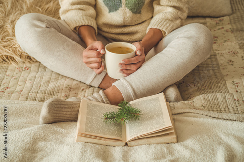 Cozy home. Beautiful girl is reading a book on the bed. Good morning with tea. Pretty young girl relaxing. The concept of reading