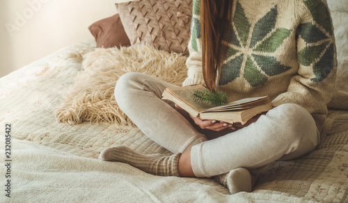 Cozy home. Beautiful girl is reading a book on the bed. Good morning with tea. Pretty young girl relaxing. The concept of reading