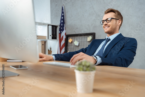 smiling businessman in eyeglasses working at table with computer monitor in office
