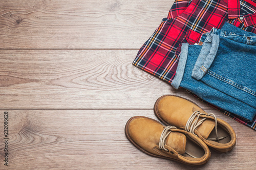Checkered shirt, jeans and yellow boots on a wooden background. Top view