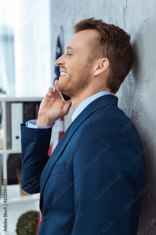 side view of happy businessman in suit talking on smartphone in modern office side view of happy businessman in suit talking on smartphone in modern office