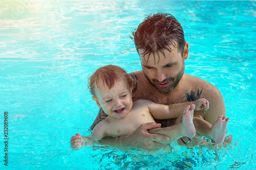 Father and child are having fun in pool. Dad and son are swimming indoor pool. Father teachs son to swim. Concept of kids sport, family summer vacation. Concept of healthy holiday and family activity.