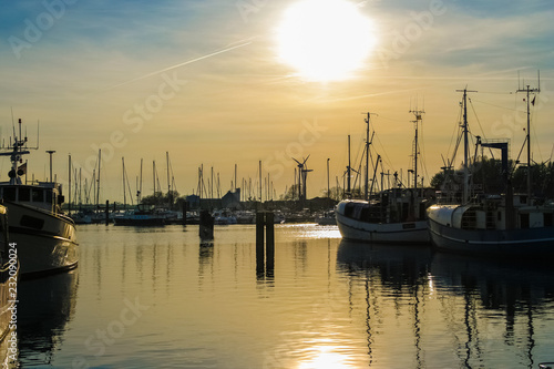 Beautiful sunset view with the silhouettes of several sailing boats and the sparkling water reflection at a harbour on Fehmarn island in Germany. 