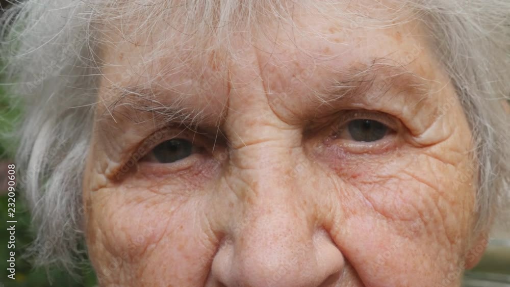 Old woman puts on glasses and looking at camera. Granny wearing eyeglasses outside. Portrait of sad grandmother outdoor. Close up Slow motion Old woman puts on glasses and looking at camera. Granny wearing eyeglasses outside. Portrait of sad grandmother outdoor. Close up Slow motion