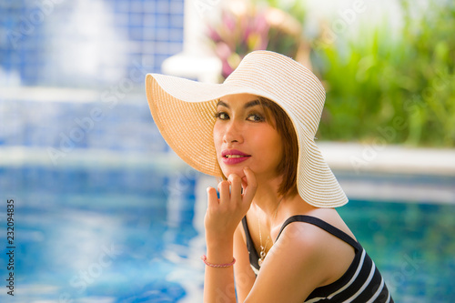 lifestyle portrait of young happy and beautiful tourist woman in Summer hat posing relaxed and smiling cheerful at tropical resort swimming pool in holidays travel