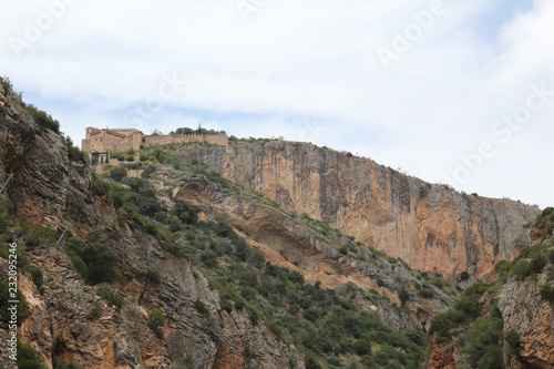The rural Alquezar town over a hill as seen from the Vero river canyon during a summer day, with the typical red rock scarp, in Alquezar, Spain